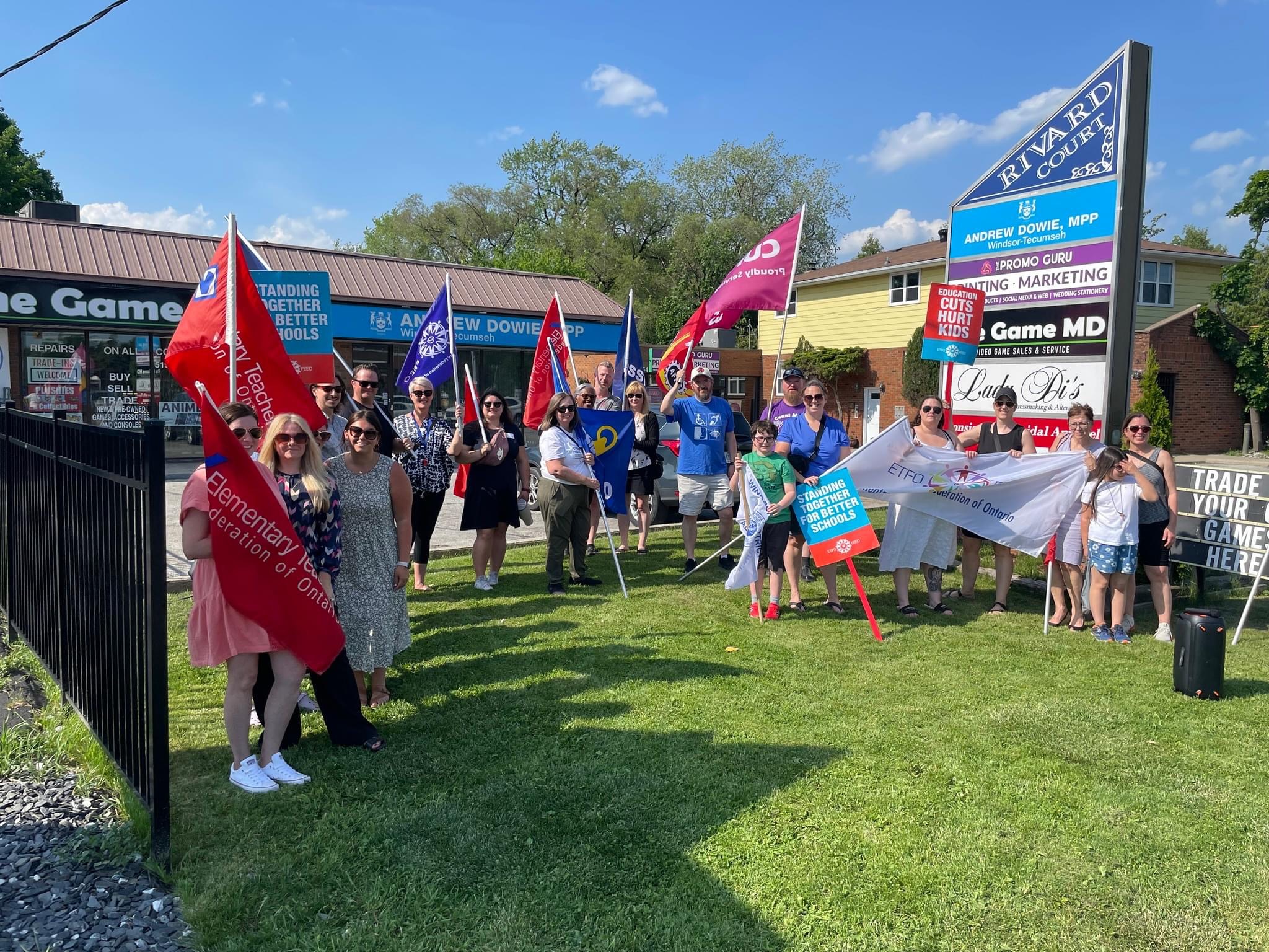 Members and education workers holding flags outside a constituency office